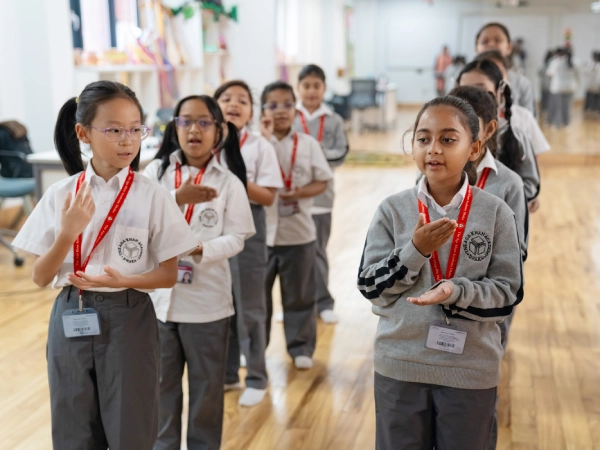 Students in uniform, standing in two rows, practise rhythmic movements in a classroom.